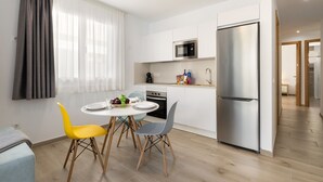 Una cocina moderna con armarios blancos, un refrigerador de acero inoxidable y una zona de comedor con una mesa redonda y dos sillas.