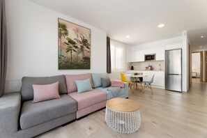 Ein modernes Wohnzimmer mit einem grauen Sofa, einem runden Couchtisch und einer Küche im Hintergrund.