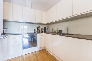 A modern kitchen with white cabinetry, a stainless steel dishwasher, and a built-in oven. - Modern 1BDR Near Heathrow with Parking Amenities (Surrey)