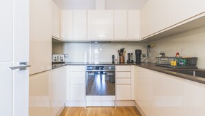 A modern kitchen with white cabinetry, a built-in oven, and a countertop with various appliances and utensils. - Modern 1BDR Near Heathrow with Parking Amenities (Surrey)
