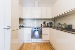 A modern kitchen with white cabinetry, a built-in oven, and a countertop with various appliances and utensils. - Modern 1BDR Near Heathrow with Parking Amenities (Surrey)
