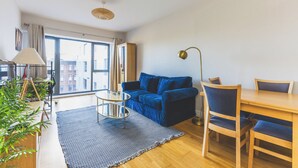 A modern living room with a sofa, a dining table, chairs, a lamp, and a view of the outside. - Modern 1BDR Near Heathrow with Parking Amenities (Surrey)