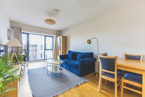 A modern living room with a sofa, a dining table, chairs, a lamp, and a view of the outside. - Modern 1BDR Near Heathrow with Parking Amenities (Surrey)