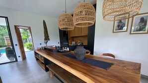 Een moderne eetruimte met een houten tafel, bankjes, rieten hanglampen en uitzicht op het omliggende landschap.