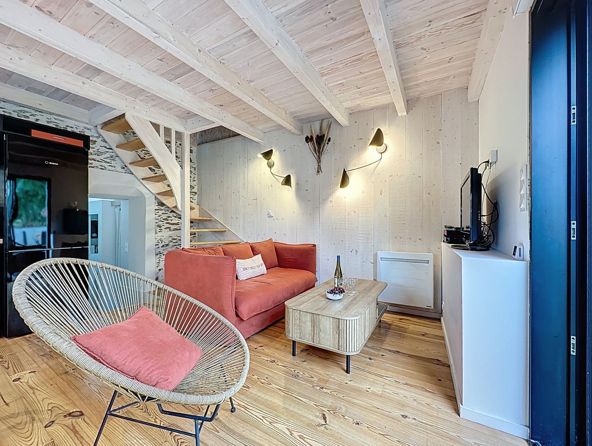 Un salon moderne avec un canapé, un fauteuil en osier, une table basse et un escalier.
