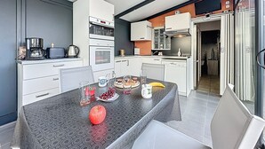 Et moderne køkken med hvide skabe, en indbygget ovn og et spiseområde med et bord dækket til to personer.
