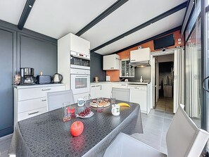 Une cuisine moderne avec des armoires blanches, un four encastré et un coin repas avec une table mise pour deux personnes.