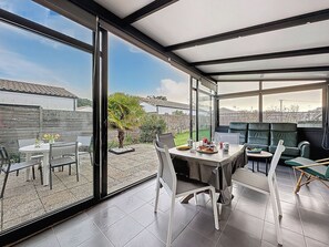 Eine überdachte Terrasse mit Esstisch, Stühlen und einer Sitzecke mit Kissen.