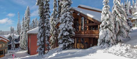 Un grand chalet en bois doté d’un balcon, entouré d’arbres couverts de neige.