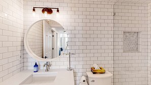 A bathroom with white subway tiles, a round mirror, a sink, a toilet, and a towel dispenser. - Okanagan - Ice and Cozy #116C (Beaverdell)