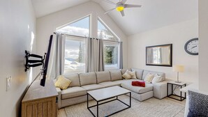 Uma sala de estar moderna com uma janela grande, um ventilador de teto, um sofá, uma mesa de centro e um relógio na parede.
