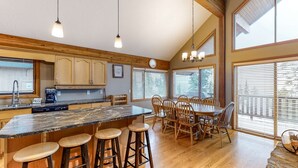 A spacious kitchen with wooden cabinets, a large island with stools, and a dining area with a wooden table and chairs. - Okanagan - Powder Paradise (Big White Mountain)