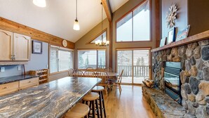 A spacious kitchen with a large island, wooden cabinets, and a stone fireplace. - Okanagan - Powder Paradise (Big White Mountain)