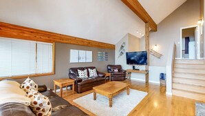 A spacious living room with a large sofa, a coffee table, and a television. There is a staircase leading to another level. - Okanagan - Powder Paradise (Big White Mountain)
