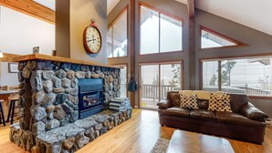 A spacious living room with a stone fireplace, leather sofa, and large windows offering views of the outdoors. - Okanagan - Powder Paradise (Big White Mountain)