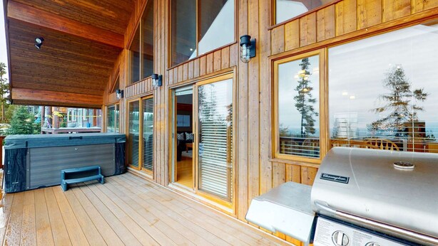 A wooden deck with a hot tub, grill, and sliding glass doors leading to an interior space. - Okanagan - Powder Paradise (Big White Mountain)