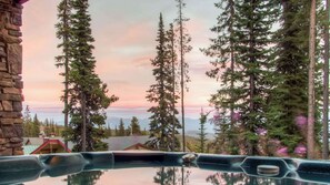 Une vue depuis un bain à remous, avec de grands pins en premier plan et une montagne en arrière-plan.