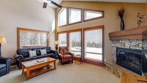 A living room with a fireplace, leather furniture, and large windows. - Okanagan - Spyglass 4C (Beaverdell)