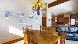 A dining area with a wooden table and chairs, a chandelier, and winter-themed wall art. - Okanagan - Spyglass 4C (Beaverdell)