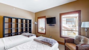Una habitación de hotel con dos camas, televisor, una silla y ventanas amplias.