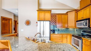 A kitchen with wooden cabinets, a stainless steel refrigerator, a microwave, and a granite countertop. - Okanagan - Spyglass 4C (Beaverdell)