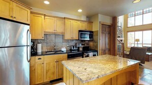 Una cocina con armarios de madera, electrodomésticos de acero inoxidable, encimera de granito y vistas al exterior a través de amplias ventanas.