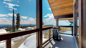 Una terraza de madera con una parrilla, con vistas a un paisaje nevado con montañas y árboles.