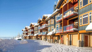 A row of multi-story wooden buildings with balconies, set against a snowy landscape. - Okanagan - Timber Ridge 17 (Kootenay Boundary E)