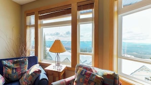 A cozy room with a large window, a lamp, and two patterned armchairs. - Okanagan - Timber Ridge 17 (Kootenay Boundary E)