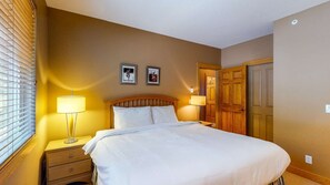 Ein Hotelzimmer mit Bett, Nachttischlampen, einem Nachttisch, einer Holztür und zwei gerahmten Bildern an der Wand.