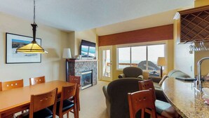 A dining area with a wooden table and chairs, a stone fireplace, and a television mounted above it. - Okanagan - Trappers Crossing 28 (Big White Mountain)