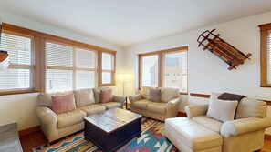 Ein Wohnzimmer mit drei Ledersofas, einem Couchtisch und einem farbenfrohen Teppich.