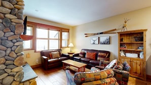 A cozy living room with a stone wall, leather sofas, a wooden coffee table, and a bookshelf. - Okanagan - Tree Tops 10 (Big White Mountain)