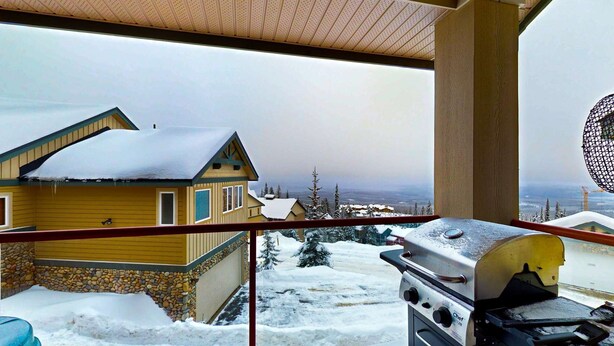 A balcony with a view of a snow-covered landscape, a stone wall, and a barbecue grill. - Okanagan - Tree Tops 10 (Big White Mountain)