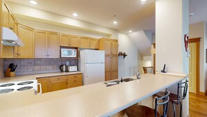A modern kitchen with wooden cabinets, a large island, a microwave, a refrigerator, and a stove. - Okanagan - Tree Tops 10 (Big White Mountain)