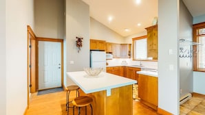 A kitchen with wooden cabinets, a white countertop, and a built-in island with stools. - Okanagan - Tree Tops 13 (Beaverdell)