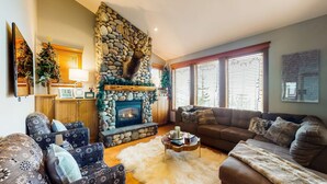 A cozy living room with a stone fireplace, comfortable seating, and large windows. - Okanagan - Tree Tops 13 (Beaverdell)