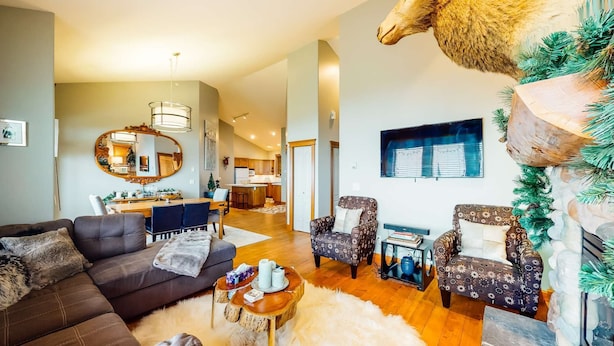 A spacious living room with a dark brown sofa, patterned armchairs, and a coffee table. A large mirror and artwork adorn the walls. - Okanagan - Tree Tops 13 (Beaverdell)