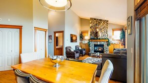 A cozy living room with a stone fireplace, comfortable seating, and a dining area with a wooden table. - Okanagan - Tree Tops 13 (Beaverdell)