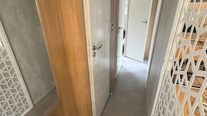 En hall med en dörr av trä, en vit avskärmning med ett geometriskt mönster och en beige bänk.