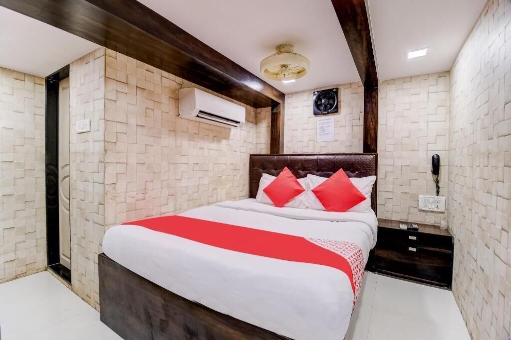 A hotel room with a bed, a nightstand, an air conditioning unit, and a wall-mounted fan.