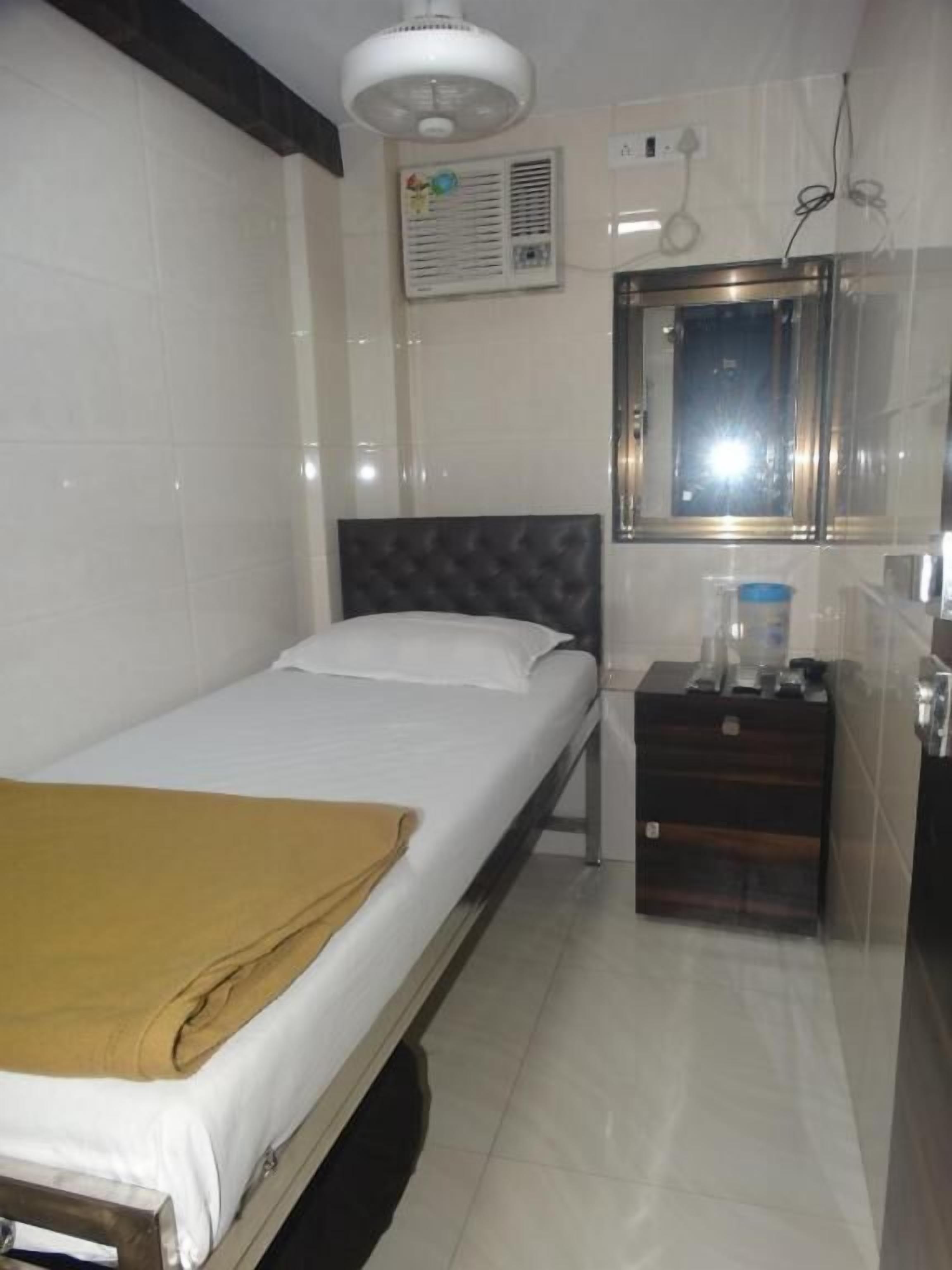 A hotel room with a bed, a bedside table, a mirror, an air conditioning unit, and a window.