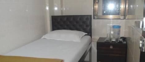 A hotel room with a bed, a bedside table, a mirror, an air conditioning unit, and a window.