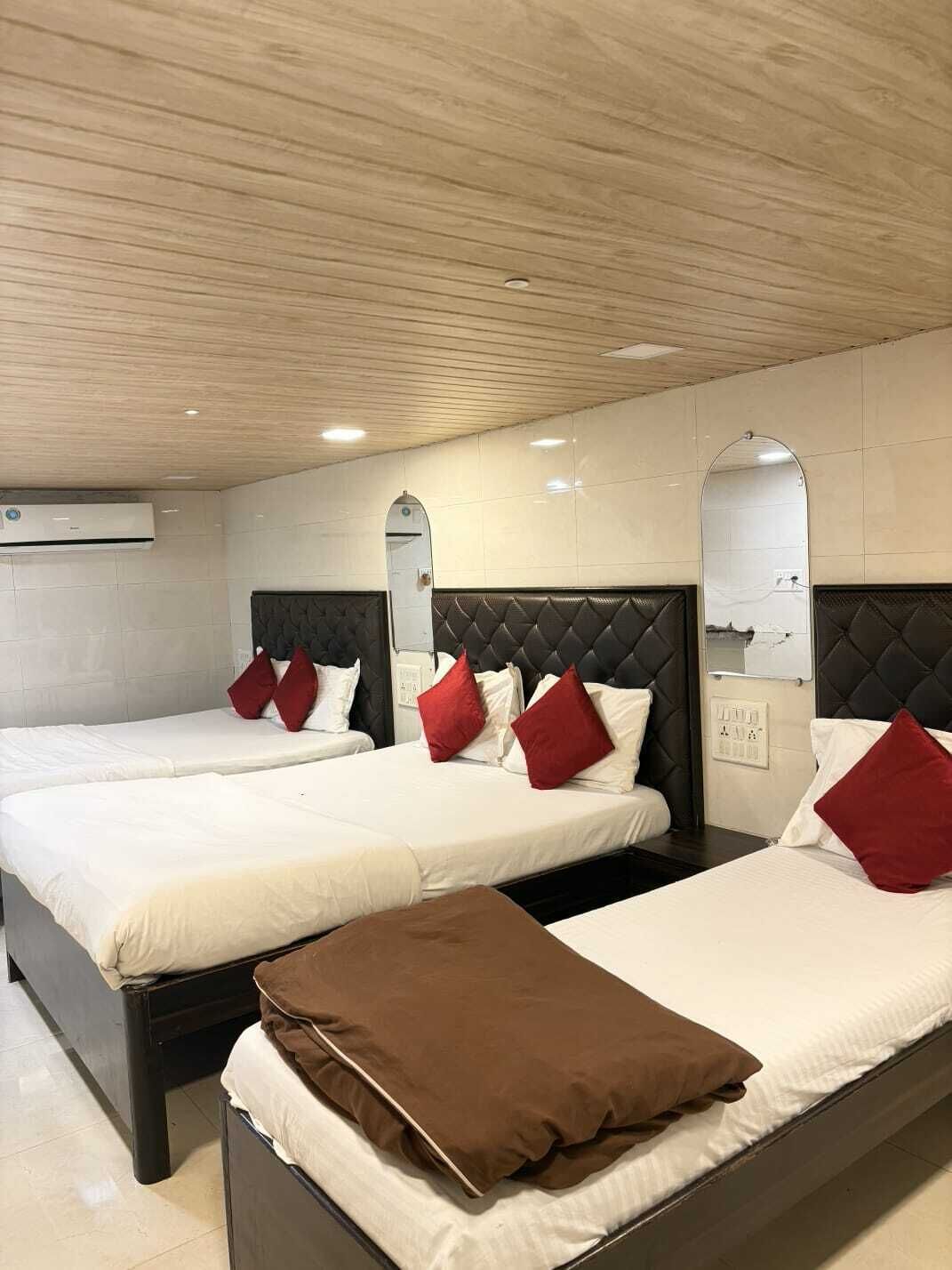 A hotel room with three beds, each with white bedding and red pillows. The room has a wooden ceiling and tiled walls.