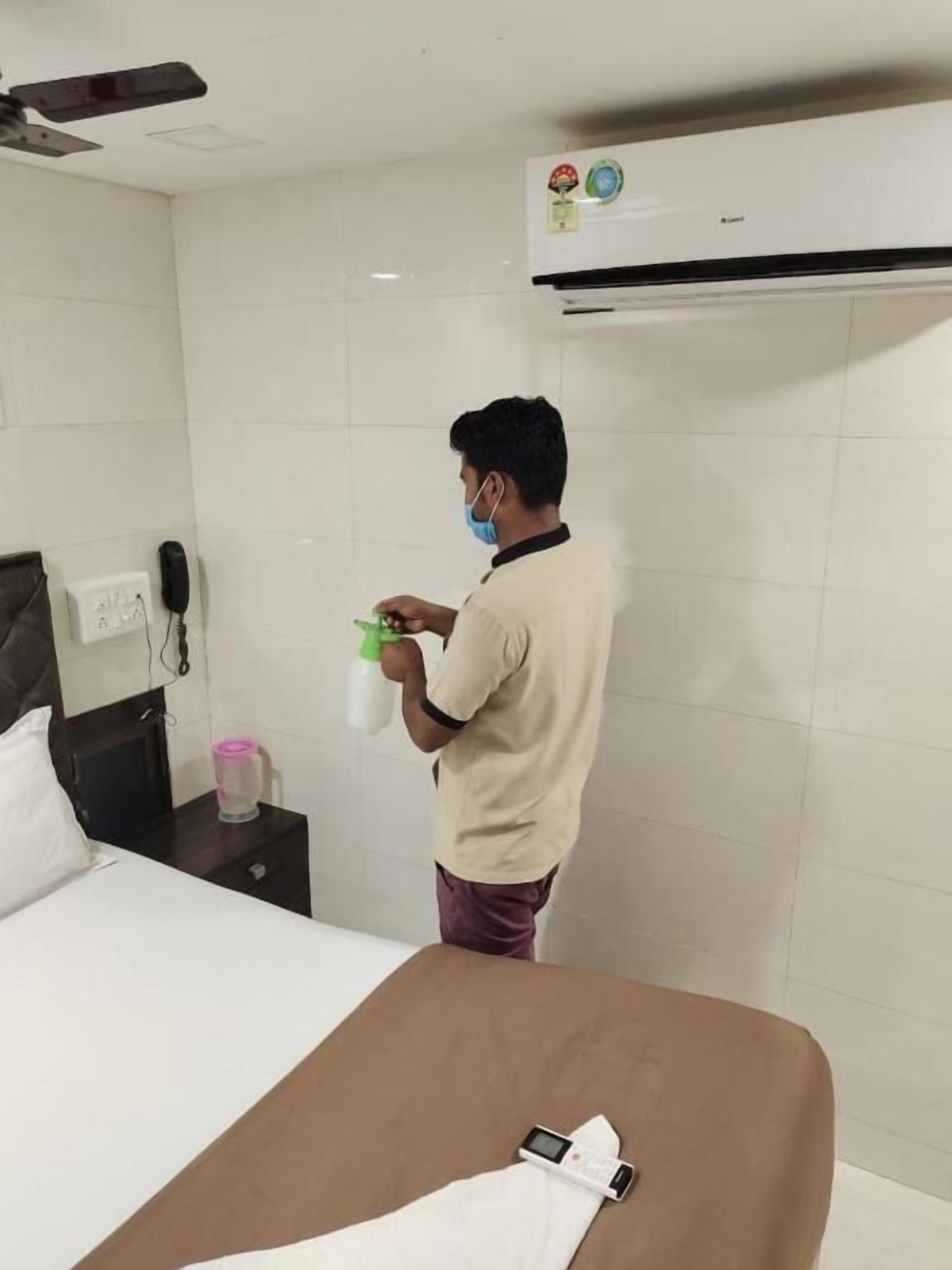 Ein Hotelzimmer mit einem Bett, einem Nachttisch mit Telefon und Wasserflasche sowie einer Wand-Klimaanlage.