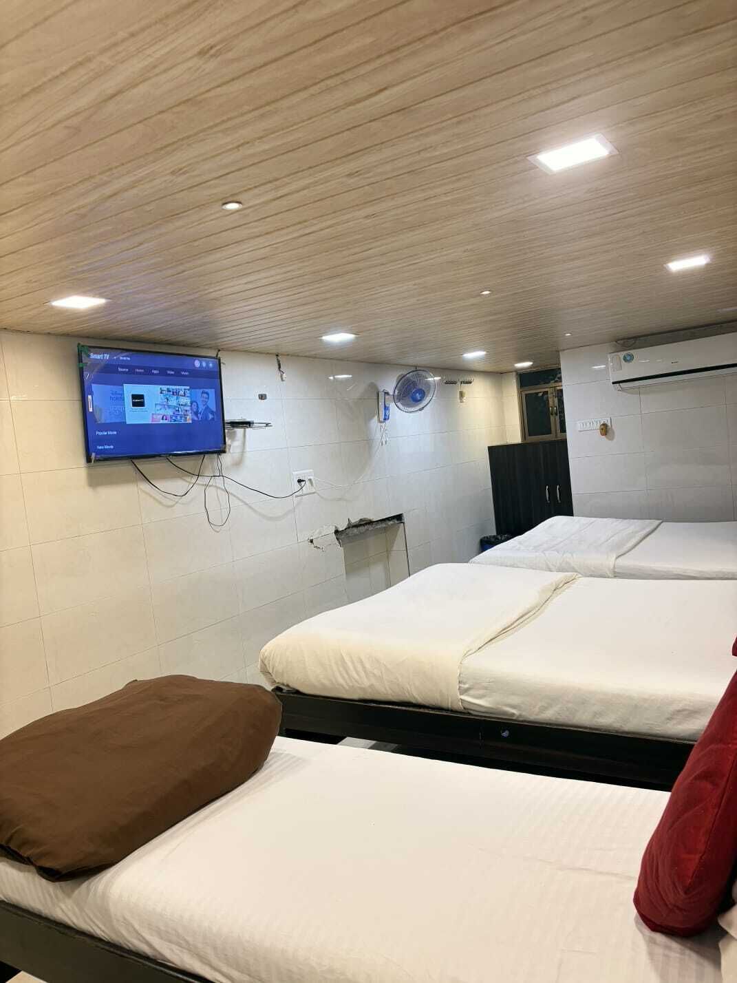 Une chambre d’hôtel avec deux lits, un téléviseur fixé au mur et un ventilateur de plafond.
