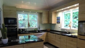 A modern kitchen with wooden cabinets, a black countertop, and a window providing a view of greenery. - Villa 5 stars Prestige Heated pool Biscarrosse Lac Golf for 6 persons (Biscarrosse)