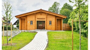 Un chalet en bois doté d’une entrée pavée, entouré de verdure et d’arbres.