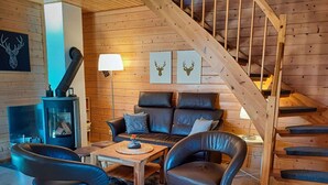 L’intérieur d’un chalet accueillant, avec un canapé, deux fauteuils, un escalier en bois et une cheminée.