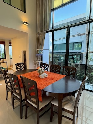 Un coin repas comprenant une table ronde, six chaises et une fenêtre donnant sur un bâtiment et sur la verdure environnante.